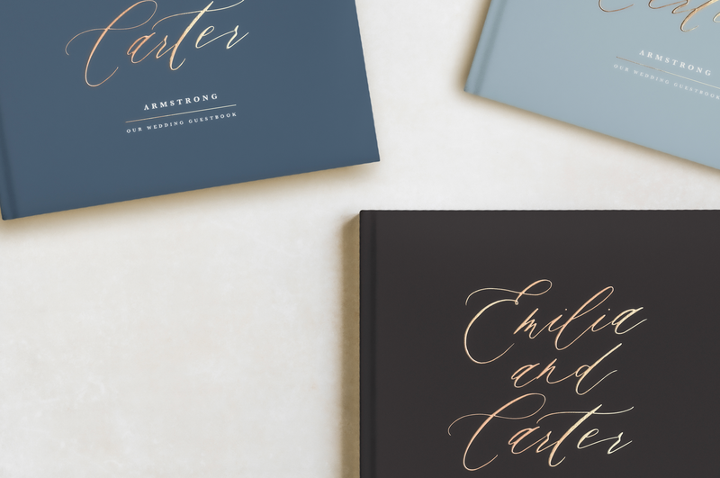 three blue and charcoal hard cover guest books with gold lettering that reads "Emilia and Carter"