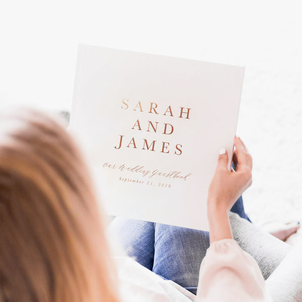 woman with red hair holding a hard cover guest book that reads "Sarah and James, our wedding guest book"